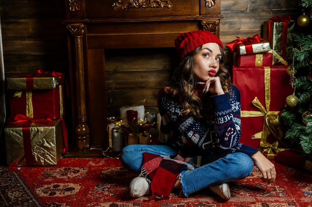 Una hermosa morena se sienta debajo de un árbol de Navidad con el telón de fondo de las decoraciones de Año Nuevo