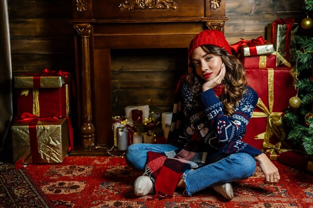 Una hermosa morena se sienta debajo de un árbol de Navidad con el telón de fondo de las decoraciones de Año Nuevo