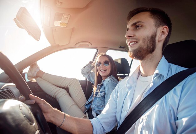 Hermosa morena sonriente relajándose con las piernas estiradas hacia la ventana mientras su novio conduce un auto