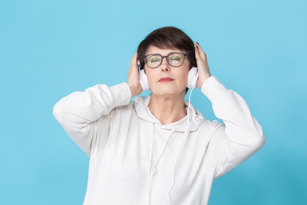 Hermosa mujer de 40-50 años escuchando música en grandes auriculares en la pared azul.