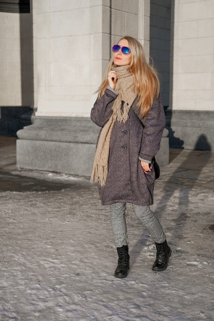 Foto una hermosa mujer con un abrigo gris y gafas de sol camina por la calle de la ciudad.