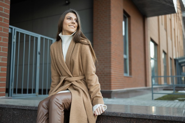 Hermosa mujer con un abrigo marrón se sienta en medio de la calle