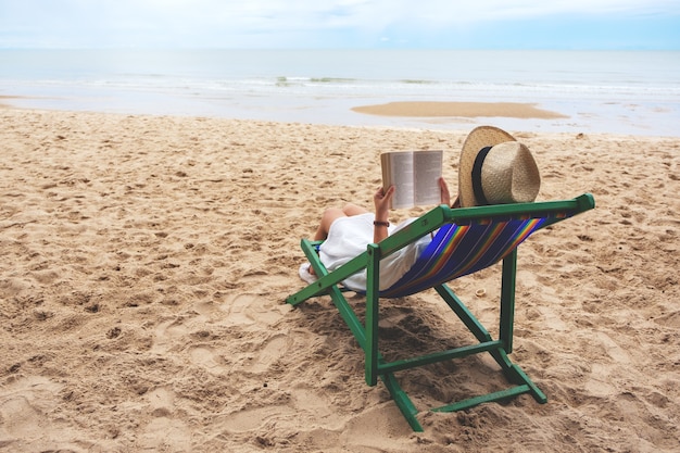 Foto una hermosa mujer acostada y leyendo un libro en la silla de playa con una sensación relajada