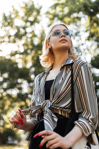 Hermosa mujer adolescente con gafas de sol en camisa vintage de moda y vestido negro camina en el parque