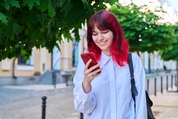 Hermosa mujer adolescente sonriente mirando el teléfono en la calle de la ciudad
