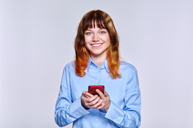 Hermosa mujer adolescente sonriente con teléfono inteligente en sus manos mirando a la cámara