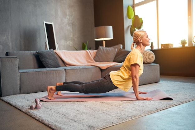 Hermosa mujer adulta atlética haciendo asanas en yoga Entrenamiento en casa Vista lateral entrenamiento de resistencia equilibrio fortalecimiento muscular