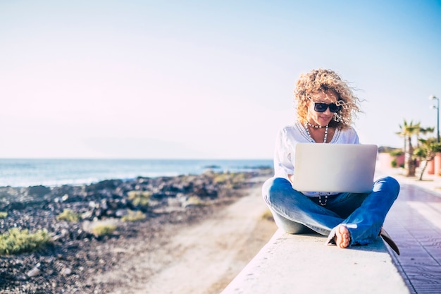 Hermosa mujer adulta caucásica con ordenador portátil de tecnología moderna en la playa al aire libre