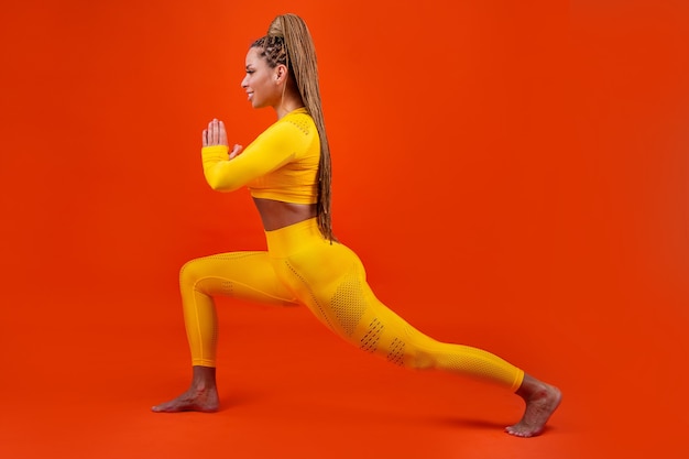 Hermosa mujer adulta en chándal amarillo sobre fondo rojo en pose de yoga