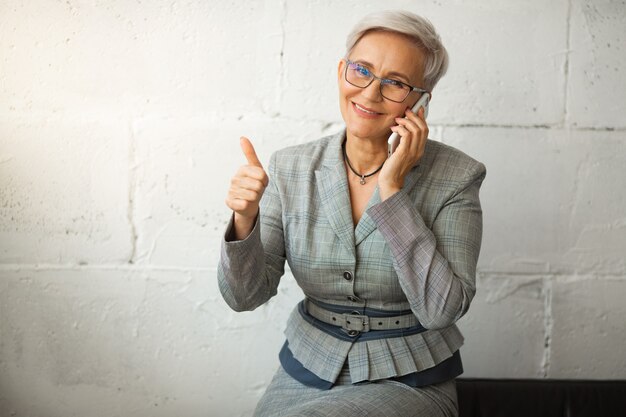 Foto hermosa mujer adulta con estilo en traje con teléfono, con gesto de mano