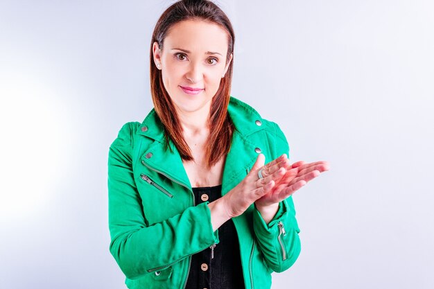 Hermosa mujer adulta joven en chaqueta verde aplaudiendo sonriendo con fondo blanco con copyspace.