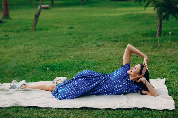 Hermosa mujer adulta joven en vestido azul picnic en la pradera en el parque