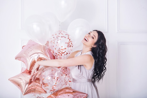 Hermosa mujer adulta joven en vestido largo de fiesta de moda con globos de color rosa