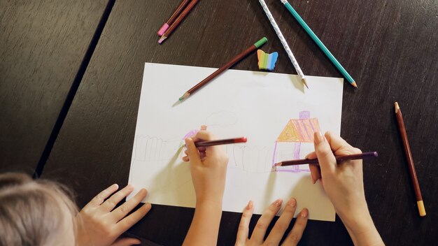 Foto hermosa mujer adulta y niña pintando con lápices sobre papel sentado en la mesa en casa, vista superior