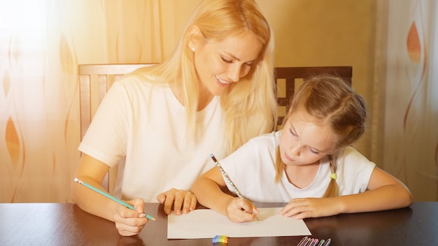 Hermosa mujer adulta y niña pintando con lápices sobre papel sentado en la mesa en casa