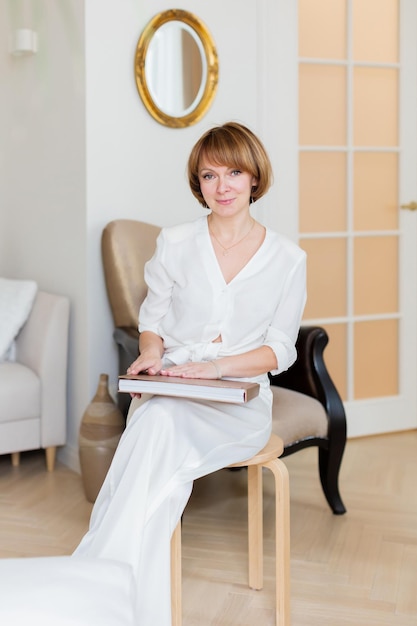 Una hermosa mujer adulta pasa tiempo en su elegante sala de estar y sostiene un gran libro en sus manos