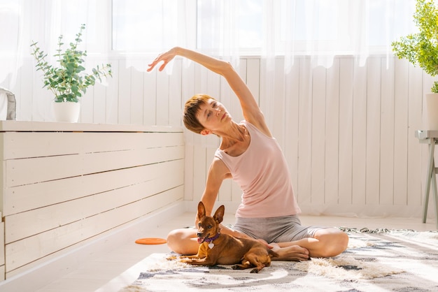 Hermosa mujer adulta practicando pose de yoga con perro pinscher pigmeo disfrutando