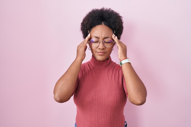 Hermosa mujer africana con el pelo rizado sobre fondo rosa con dolor de cabeza en la cabeza porque el estrés sufre migraña