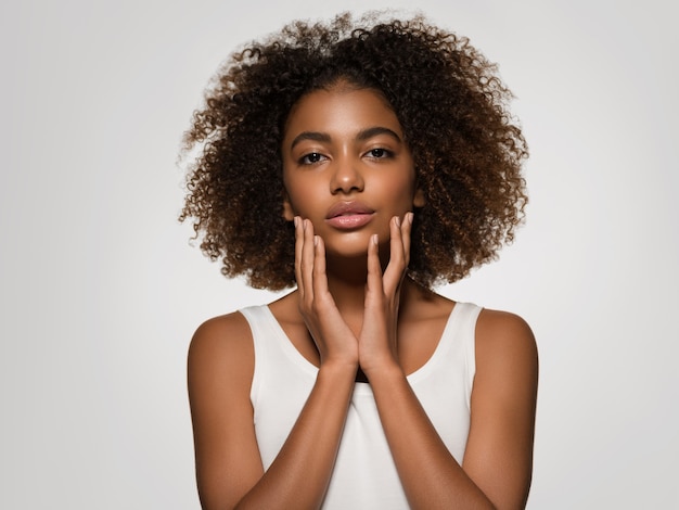 Hermosa mujer africana retrato de camiseta blanca corte de pelo afro tocando su cara Color de fondo gris