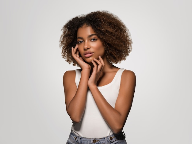 Hermosa mujer africana retrato de camiseta blanca corte de pelo afro tocando su cara Color de fondo gris