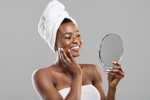 Hermosa mujer africana sosteniendo un espejo y tocando su piel suave y perfecta