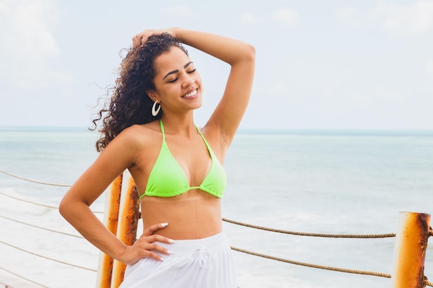 Foto hermosa mujer afro negra con bikini brasileño latinoamericano con la espalda sonriendo en un resort mirando las olas del mar rompiendo