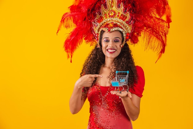 Hermosa mujer afro en traje de carnaval y samba con mini carrito de supermercado en la mano. Concepto de compras de carnaval. promoción de carnaval