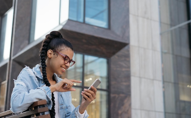 Hermosa mujer afroamericana con anteojos elegantes con comunicación de teléfono inteligente en línea