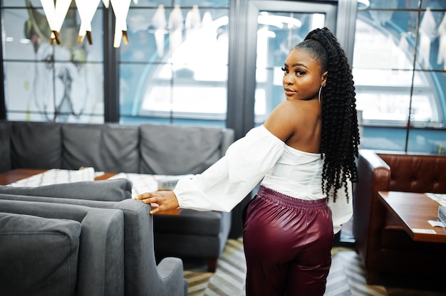 Hermosa mujer afroamericana en blusa blanca y pantalones de cuero rojo posan en el restaurante.