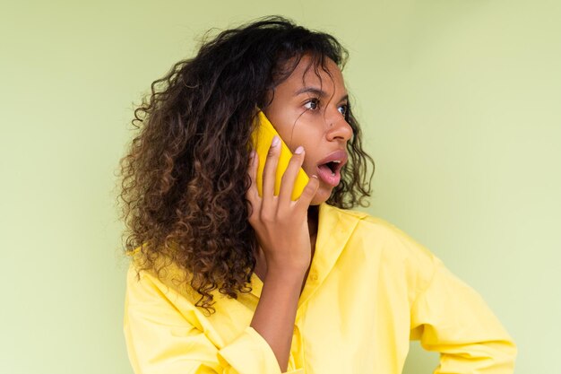 Hermosa mujer afroamericana en camisa casual sobre fondo verde hablar por teléfono móvil sorprendido co