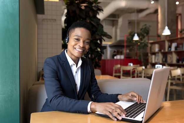 Hermosa mujer afroamericana mirando a la cámara y sonriendo trabajando en comunicación de video de café de coworking usando auriculares mujer de negocios independiente