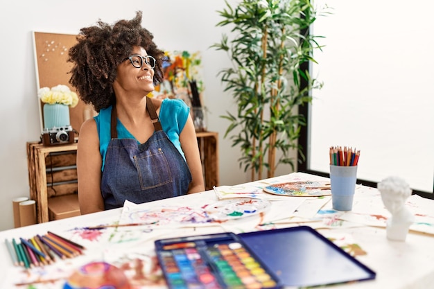 Hermosa mujer afroamericana con pintura de cabello afro en el estudio de arte mirando de lado a lado con una sonrisa en la cara expresión natural riendo confiada