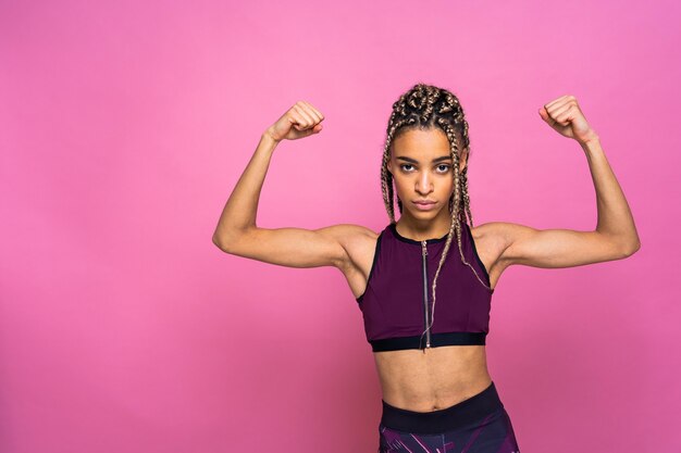 Hermosa mujer afroamericana con retrato de coletas en la pared de color haciendo ejercicios deportivos