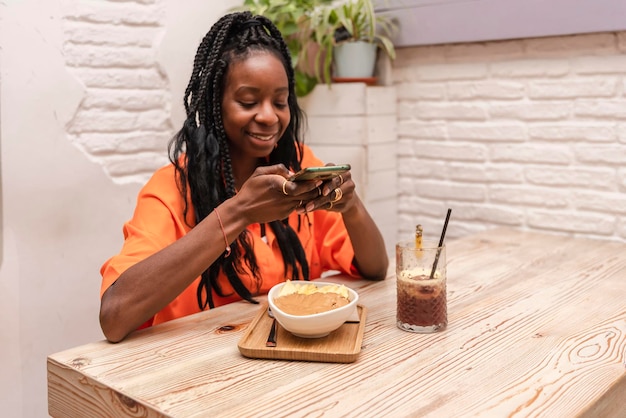 Una hermosa mujer afroamericana sentada en un bar tomando una foto de un tazón de acai con mantequilla de maní