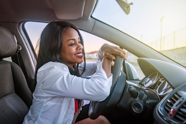 Hermosa mujer afroamericana sonriente dentro de un automóvil apoyado en el volante