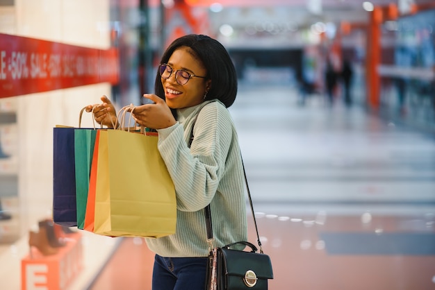 Hermosa mujer afroamericana sosteniendo bolsas multicolores en una tienda.