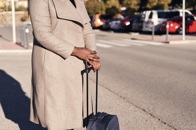Hermosa mujer afroamericana sosteniendo una maleta y mirando el reloj de pulsera