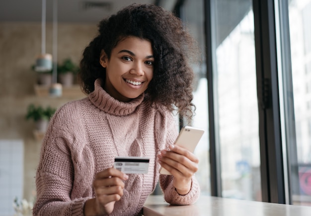 Hermosa mujer afroamericana con tarjeta de crédito, haciendo pagos, compras en línea