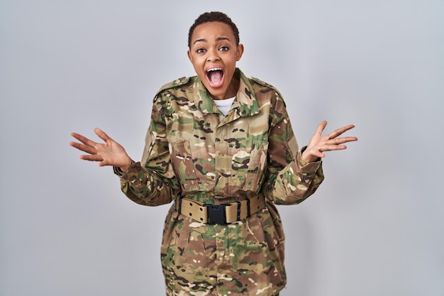 Hermosa mujer afroamericana con uniforme del ejército de camuflaje celebrando loca y sorprendida por el éxito con los brazos levantados y los ojos abiertos gritando emocionados. concepto de ganador