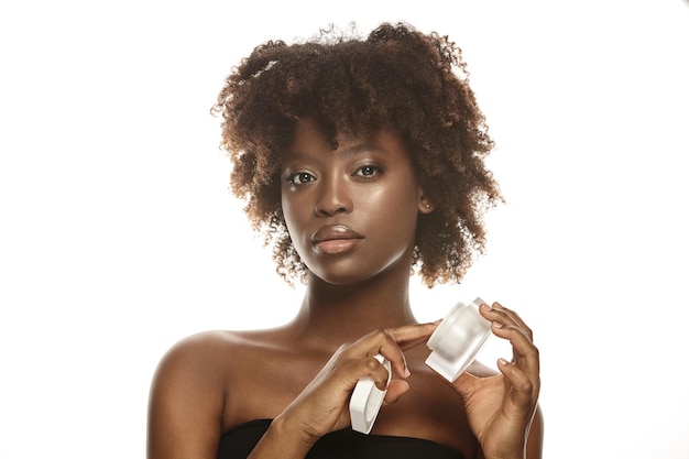 Hermosa mujer afroamericana usando crema hidratante facial en un blanco aislado