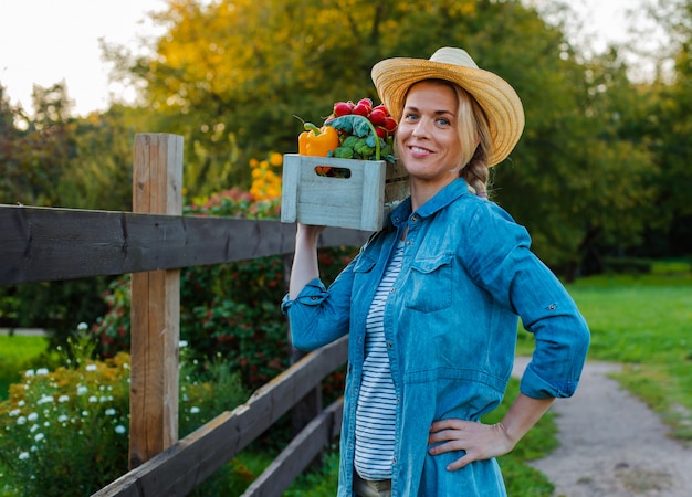 Foto hermosa mujer agricultor con sombrero con caja de verduras ecológicas frescas en el jardín