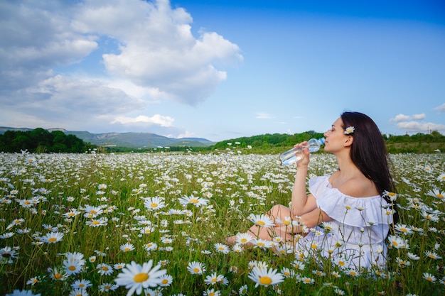 Hermosa mujer agua potable en un campo con margaritas