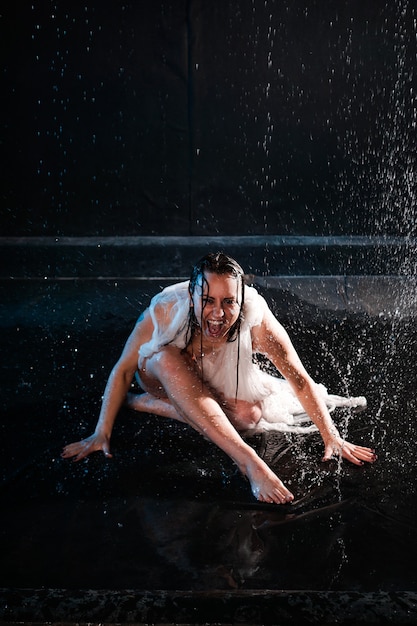 Hermosa mujer en aguamarina en tela transparente en luz de neón. La niña bajo las gotas de lluvia grita desesperada. Foto emocional