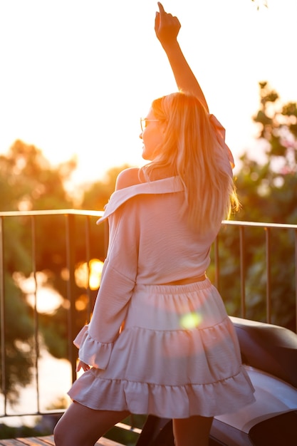 Una hermosa mujer al atardecer se encuentra en una terraza con vistas al mar. Foto de alta calidad