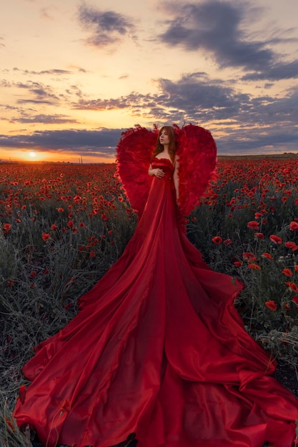 Hermosa mujer con alas rojas en el campo de amapolas