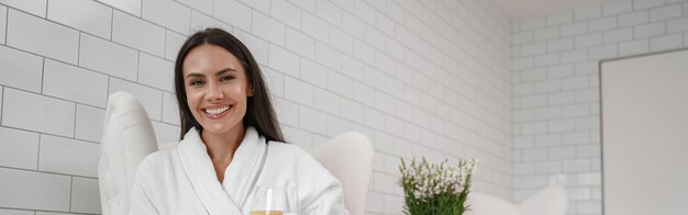 Hermosa mujer en albornoz blanco bebe agua durante el procedimiento médico en la clínica de belleza