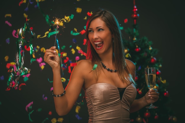 Hermosa mujer alegre celebrando el Año Nuevo. Ella se está divirtiendo con bengala y champán.