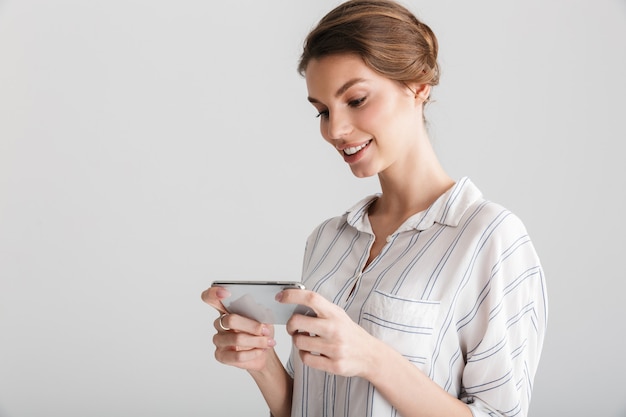 Hermosa mujer alegre sonriendo y jugando videojuegos en el teléfono celular aislado sobre fondo blanco.