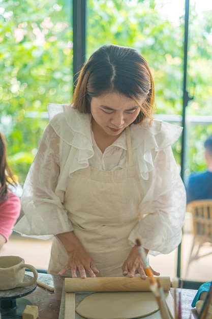 Hermosa mujer alfarera trabajando en la rueda de alfareros haciendo vasijas de cerámica de arcilla en el taller de cerámica Enfoque mano mujer joven adjuntando parte del producto de arcilla al futuro producto de cerámica Taller de cerámica