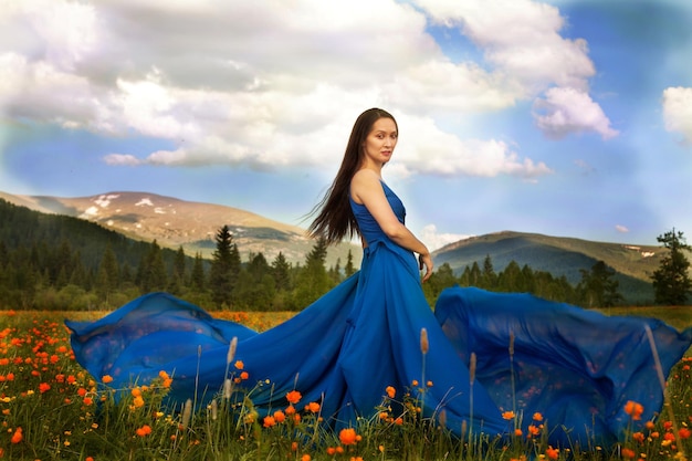 Una hermosa mujer de apariencia asiática con un vestido azul camina en un prado verde con flores naranjas en las montañas de Altai en verano. concepto de belleza, turismo.